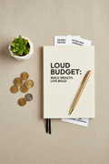 Flat lay of a budget planner, pen, coins and plant on a neutral background
